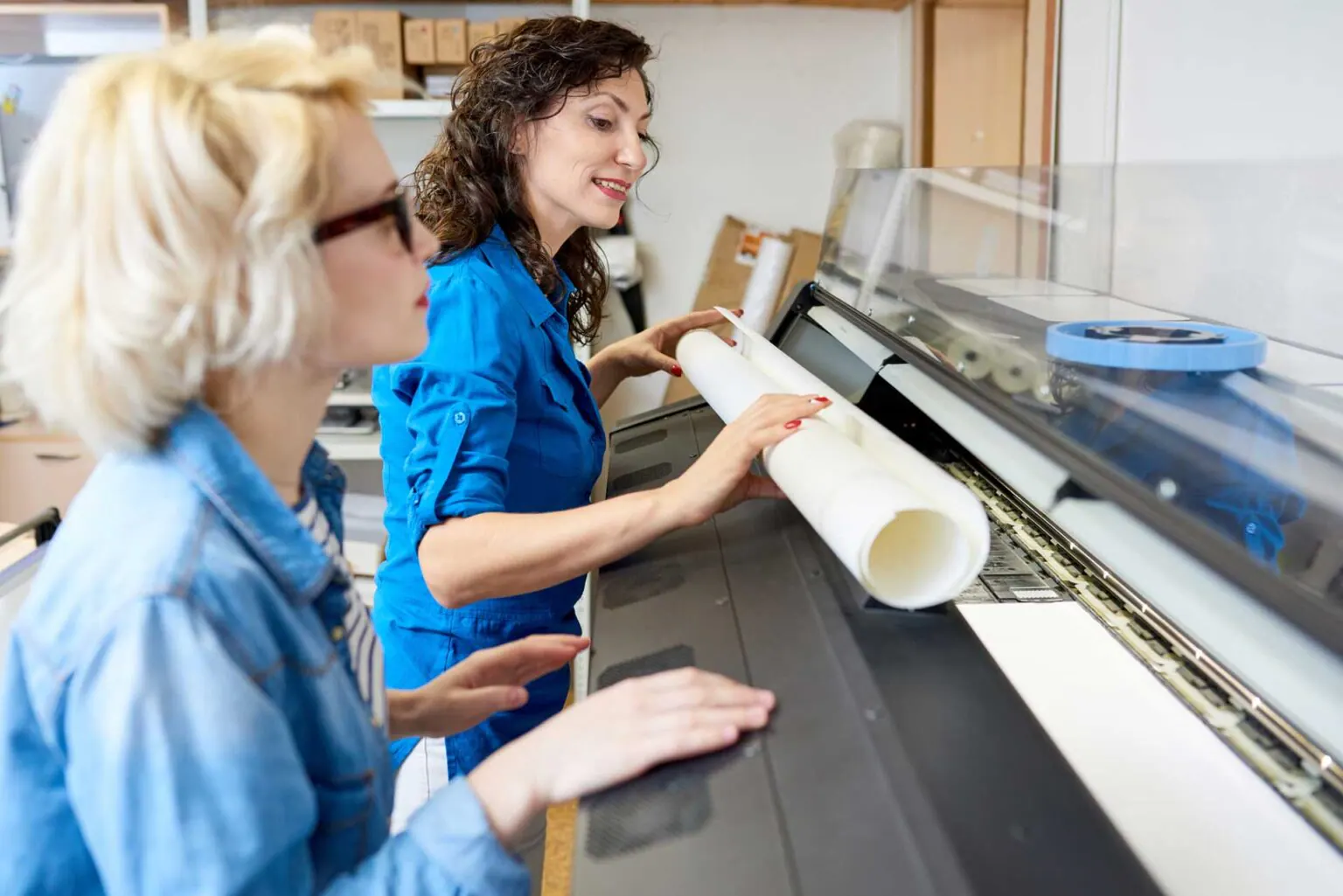 Dos profesionales cargando una bobina de papel en un plotter de impresión